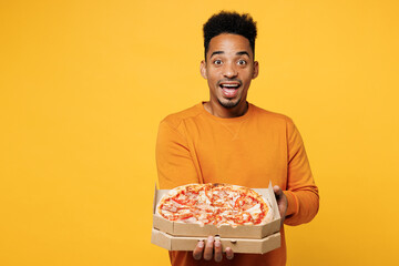Young surprised man wear orange sweatshirt casual clothes holding italian pizza in cardboard...