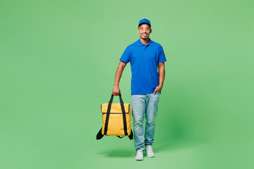 Full body smiling delivery guy employee man he wear blue cap t-shirt uniform workwear work as dealer courier hold yellow thermal food bag backpack isolated on plain green background. Service concept.
