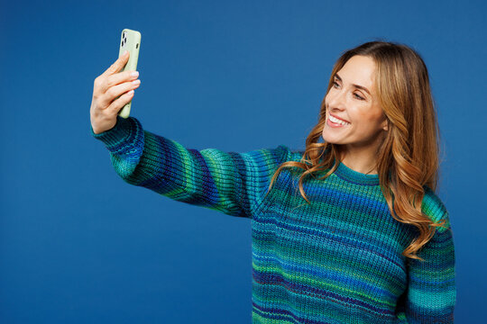 Young woman she wear knitted sweater casual clothes doing selfie shot on mobile cell phone post photo on social network isolated on plain blue cyan color background studio portrait. Lifestyle concept