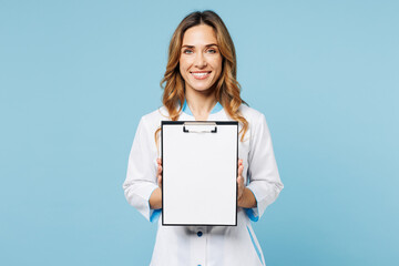 Female happy smiling doctor woman wears white gown suit work in hospital clinic office hold clipboard with blank area medical documents isolated on plain blue background. Health care medicine concept.