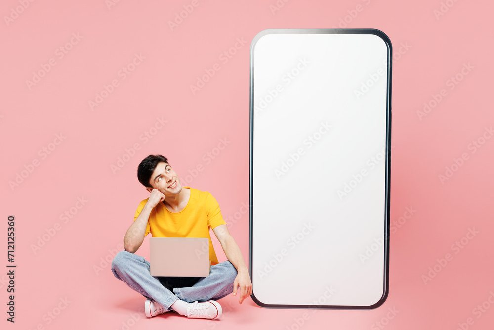 Wall mural Full body young IT man in yellow t-shirt casual clothes big huge blank screen mobile cell phone smartphone with copy space area use work on laptop pc computer isolated on plain light pink background