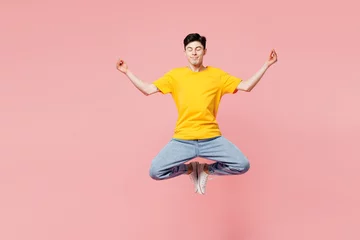  Full body young man wears yellow t-shirt casual clothes jump high hold spread hands in yoga om aum gesture relax meditate try to calm down isolated on plain pastel pink background. Lifestyle concept. © ViDi Studio