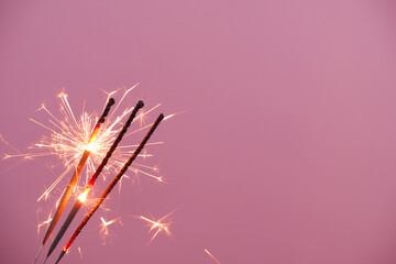 Three burning sparklers on pink background, copy space for text.	