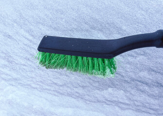 Removing snow from a car window with a brush with green bristles close-up on a sunny, frosty day....
