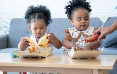 Cute African daughter eating pizza at home. Children kids enjoy and having fun with tasty lunch...