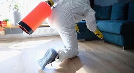 Person in hazmat suit disinfects living room with spray gun. Prevention of spread of diseases....