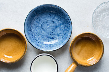 Overhead view of different plates dinnerware on a marble countertop, top view of brown ramekin, blue plate and white cup - obrazy, fototapety, plakaty