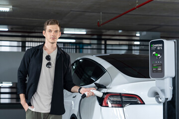 Young man travel with EV electric car to shopping center parking lot charging in downtown city...