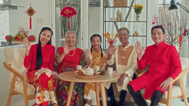 Long portrait of big multi-generational Asian family in traditional costumes waving to camera while gathering for Tet celebrationLong portrait of big multi-generational Asian family in traditional cos