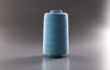 Close-up of blue colour thread spool on grey background, thread for dressmaking industry, yarn for sewing. Hobby, tailoring, atelier concept. Copy space