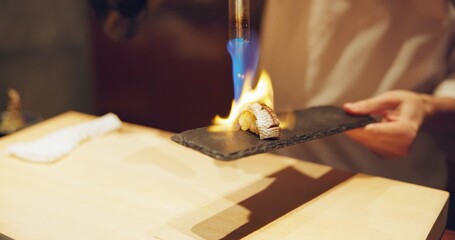 Hands, fire and cooking sushi with chef in restaurant for traditional Japanese food or cuisine closeup. Kitchen, flame for seafood preparation and person working with gourmet meal recipe ingredients