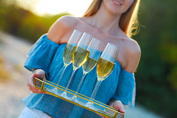 Happy woman holding tray with champagne sparkling wine into glasses outdoors at a beach