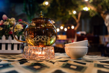 the table with a white tablecloth are transparent glass teapot and cups with green tea on the...