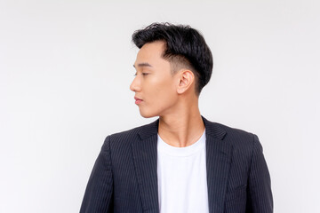 Elegant young Asian man in a suit posing with a side profile view against a white backdrop,...
