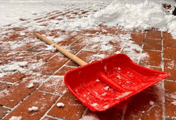 Close up of a red small snow shovel on the ground with snow 