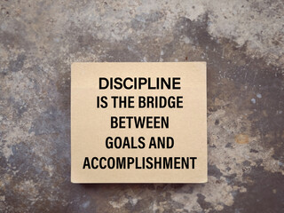 Motivational and inspirational wording. DISCIPLINE IS THE BRIDGE BETWEEN GOALS AND ACCOMPLISHMENT written on a notepad. With blurred style background.