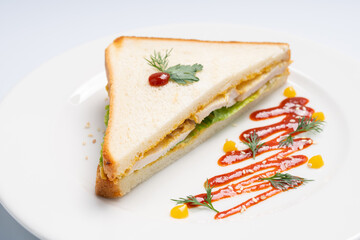 Sandwich with chicken and greens on a white plate and a white background