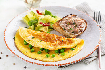 Omelette with green peas and toast with cod liver on white plate.  Frittata - italian omelet.