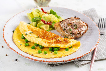 Omelette with green peas and toast with cod liver on white plate.  Frittata - italian omelet.
