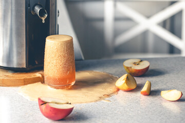 Juicer and glass filled with apple juice on the kitchen table.