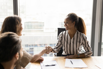 Fototapeta premium Happy confident African American businesswoman giving handshake to manager, reaching successful agreement, discussing cooperation, business partnership, contract on group meeting