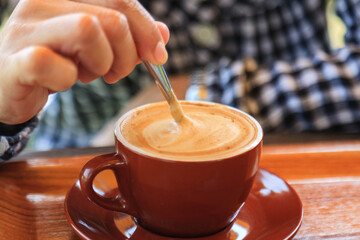 Woman's hands holding a spoon and stirring hot coffee on the table