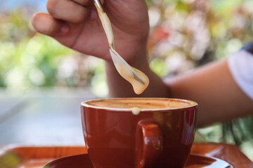 Woman's hand holding a spoon and scooping hot coffee cream foam on the table