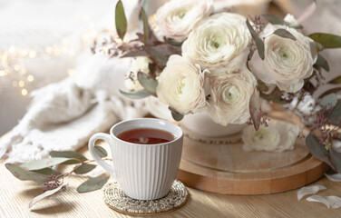 A cup of tea and a bouquet of ranunculus flowers on a blurred background.