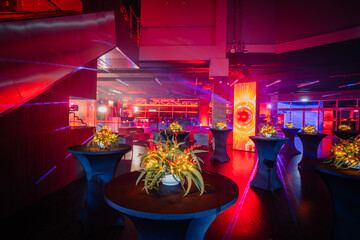  cocktail tables with floral centerpieces in a venue with dynamic red lighting and futuristic...