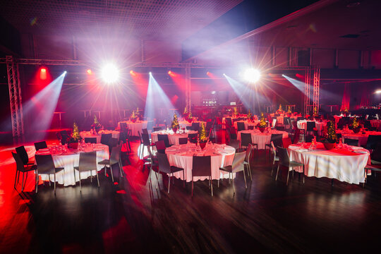  banquet hall with tables set for a festive event, illuminated by striking stage lights and spotlights.