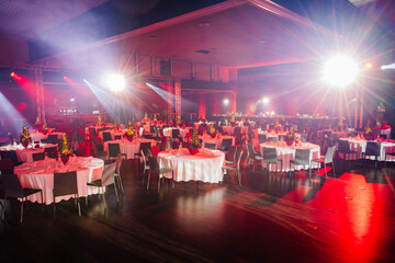  large event hall with set dining tables, festive centerpieces, and bright stage lighting...