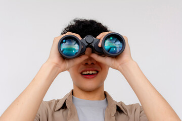 A cheerful young Asian man is using binoculars to explore, symbolizing curiosity, search, and...