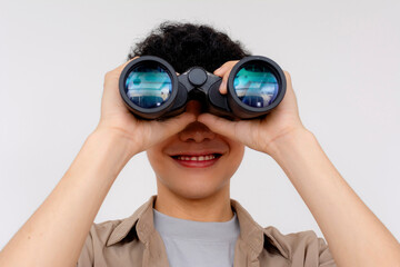 Happy young Asian adult holding binoculars in front of eyes, smiling, on a light background....