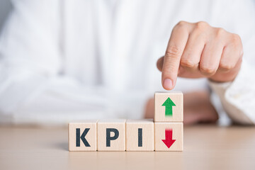 KPI or Key Performance Indicator concept. KPI text on wooden blocks with hand point on arrow up and down. Business planning for target achievement. Measure of performance for a specific objective.