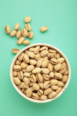 Bowl with pistachios on mint background. Vertical photo