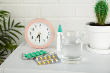 Pink alarm clock with glass of water and blister packages of pills on light table background.