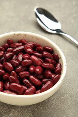Red beans in bowl and spoon on grey background.