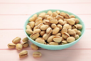Bowl with pistachios on pink wooden background.