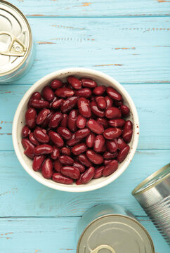 Red kidney beans in bowl and cans on blue background. Vertical photo