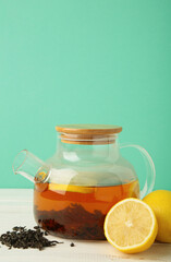 Black tea with lemon in glass teapot on mint background. Healthy drink concept.