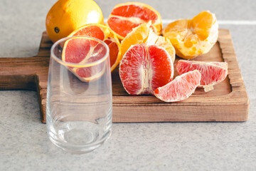 Empty glass and fresh sliced oranges on wooden board in the kitchen.