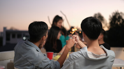 Group of friends taking and enjoying drinks during rooftop party at sunset.