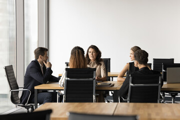 Diverse team of serious professional colleagues discussing project management issues, talking at large meeting table, brainstorming on strategy, problem solving, teamwork, discussing ideas