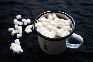 Fototapeta na wymiar Cup of cocoa with marshmallows on a black background where white marshmallows are scattered