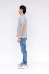 Profile view of a young Asian man in casual attire standing confidently with a white backdrop.