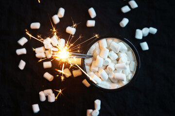 Cup of cocoa with marshmallows and sparklers on a black background where white marshmallows are...