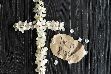 Cross with flowers on a wooden background with the inscription Christ is Risen. Easter concept. Cross symbolizing the death and resurrection of Jesus Christ