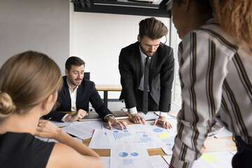Focused business team analyzing sales together, reviewing financial statistic paper reports, discussing documents, diagrams at meeting table, talking over economic graphs