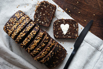 A piece of dark bread with a heart of butter next to sliced ​​bread and a knife on a linen napkin