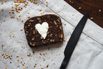 A piece of dark bread with a heart of butter next to a knife on a linen napkin